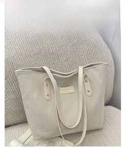 Detail of cream corduroy tote bag showing leather logo patch and gold metallic studs