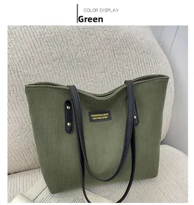 Detail of green corduroy tote bag with black leather handles on a white sofa