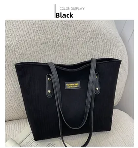 Detail of black corduroy tote bag with leather handles and yellow brand label on soft sofa