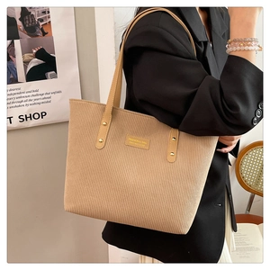 Detail of beige corduroy tote bag featuring leather logo patch and brown shoulder straps