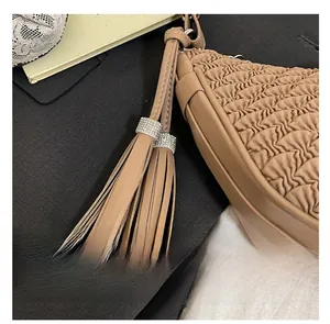 Close-up of beige pleated shoulder bag featuring dual tassels and rhinestone accents