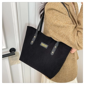 Close-up of black corduroy tote bag with gold rivet leather straps and fashion label