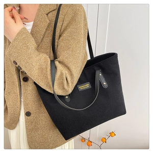 Detail of black corduroy tote bag with yellow fashion label and sturdy leather handles