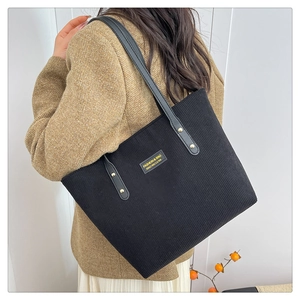 Detail of black corduroy tote bag with leather straps on a model wearing brown blazer