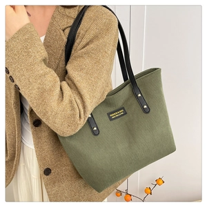 Side view of olive green corduroy tote bag with black leather strap on a model