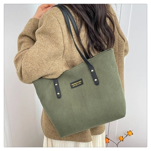 Detailed view of green corduroy tote bag with black leather strap and rivet accents