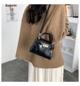 Detailed view of a black glossy handbag with gold metal clasp and leather strap accents