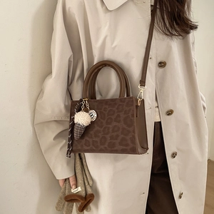 Stylish brown leopard print baguette bag with plush keychain worn on beige trench coat