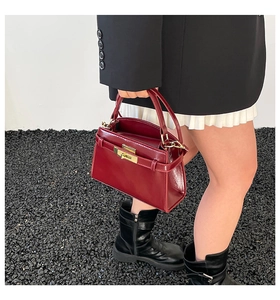 Detail of burgundy trapezoid handbag with gold twist-lock and glossy leather finish