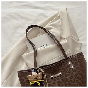 Detail of leopard print tote bag with gold logo and cute bear charm on ivory blazer