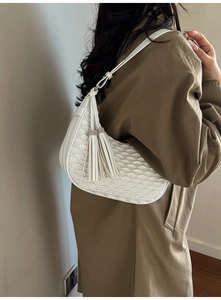 Detail of white quilted half-moon bag featuring leather tassels and rhinestone accents