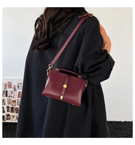 Detailed texture of burgundy crossbody bag featuring suede flap and gold metal circular buckle