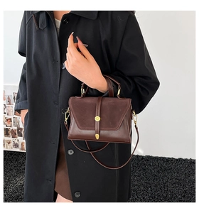 Detail of dark brown leather crossbody bag with gold round clasp and detachable strap