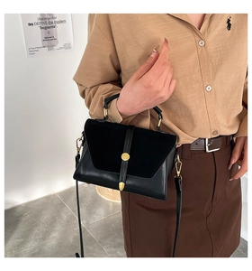 Detail of black trapezoid handbag with matte flap, golden stud, and metal bottom rivets