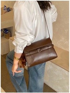 Detail view of a vintage dark brown tote bag with metal buckle strap worn by a model