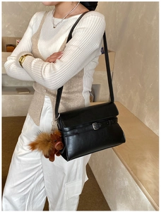 Detail of black leather shoulder bag featuring a metal buckle and cute horse charm