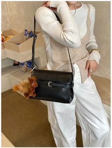 Detail of black matte leather shoulder bag with buckle strap and brown horse plush charm