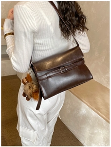 Detail of dark brown faux leather crossbody bag with decorative buckle and plush charm