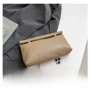 Detail shot of khaki woven texture clutch with zip closure next to office accessories