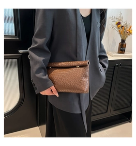 Detail of dark brown woven leather envelope clutch bag held by model in office setting