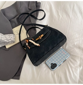 Detail of matte black retro crossbody bag featuring ethnic bead tassel and gold metal clasp