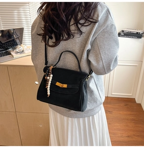 Close-up of black matte square bag with golden lock and decorative wooden beads