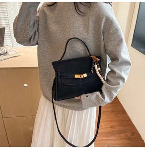 Detail of black matte square bag with gold twist lock and stylish beaded charm