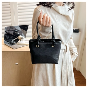 Detail of black bucket bag with canvas leather stitching and decorative knots held by model