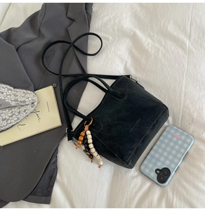 Détail du sac seau en cuir noir avec breloque ethnique perlée sur des draps blancs