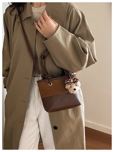 Close-up of brown two-tone patchwork tote bag with cute bear charm worn with trench coat