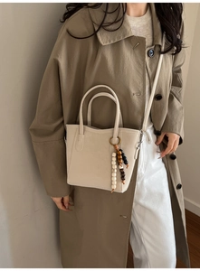 Détail du sac cabas en cuir crème avec pompon perlé et fine bandoulière réglable