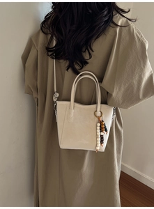 Detailed view of beige tote bag with wooden bead charm and long shoulder strap