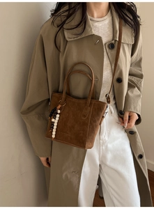 Detail of a brown suede bucket bag with a wooden bead charm and a detachable strap
