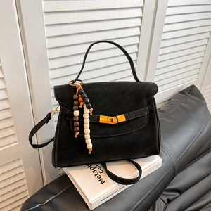 Matte black leather tote bag with gold lock and decorative wood bead charm on white books