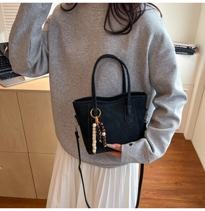 Detail of black suede bucket bag featuring long wooden bead charm and shoulder strap
