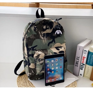 Detail of camouflage backpack with bear charm, showing capacity with tablet and books