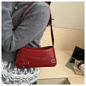 Detailed side view of a red shoulder bag featuring cross-strap design and metal buckle detail