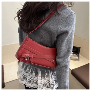 Detail of red leather shoulder bag featuring metal buckle and bow decoration on the side
