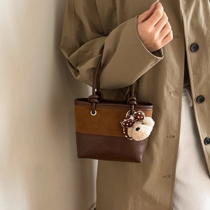 Vintage brown leather bucket bag with plush bear charm worn by a model in trench coat
