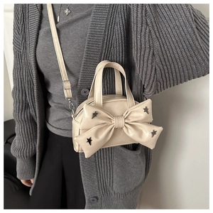 Dettaglio borsa crema con fiocco e borchie a stella su cardigan in maglia grigia