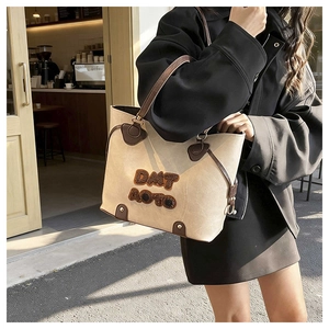 Sac fourre-tout beige et marron porté avec un costume noir dans un café cosy