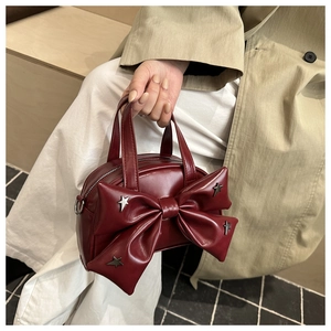 Détail d'un sac à main rouge foncé en cuir mat avec nœud et rivets étoiles argentés