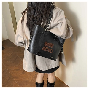 Dettaglio della borsa tote in pelle nera con toppe con lettere marroni sulla tracolla
