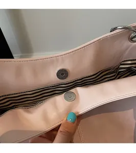 Detail of pink faux leather bag showing magnetic snap closure and striped fabric lining