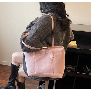 Detailed view of the pink tote bag with metal logo and long shoulder strap on model
