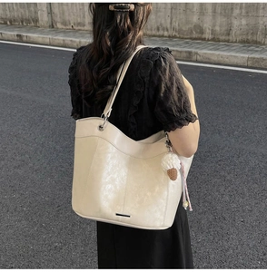 Detail view of a creamy beige tote bag with a silver metal trim and ice cream charm