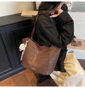 Detail view of large brown faux leather tote bag with plush charm and bow accessory