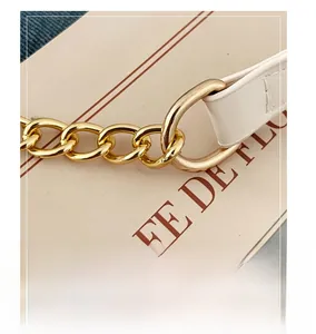 Detailed close-up of golden metal chain link attached to a white leather shoulder strap