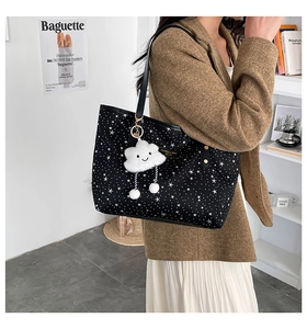 Detail of black star print tote bag with plush cloud charm on a shoulder-carried model