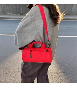 Outdoor shot of a red cylindrical fitness bag with handles and adjustable shoulder strap